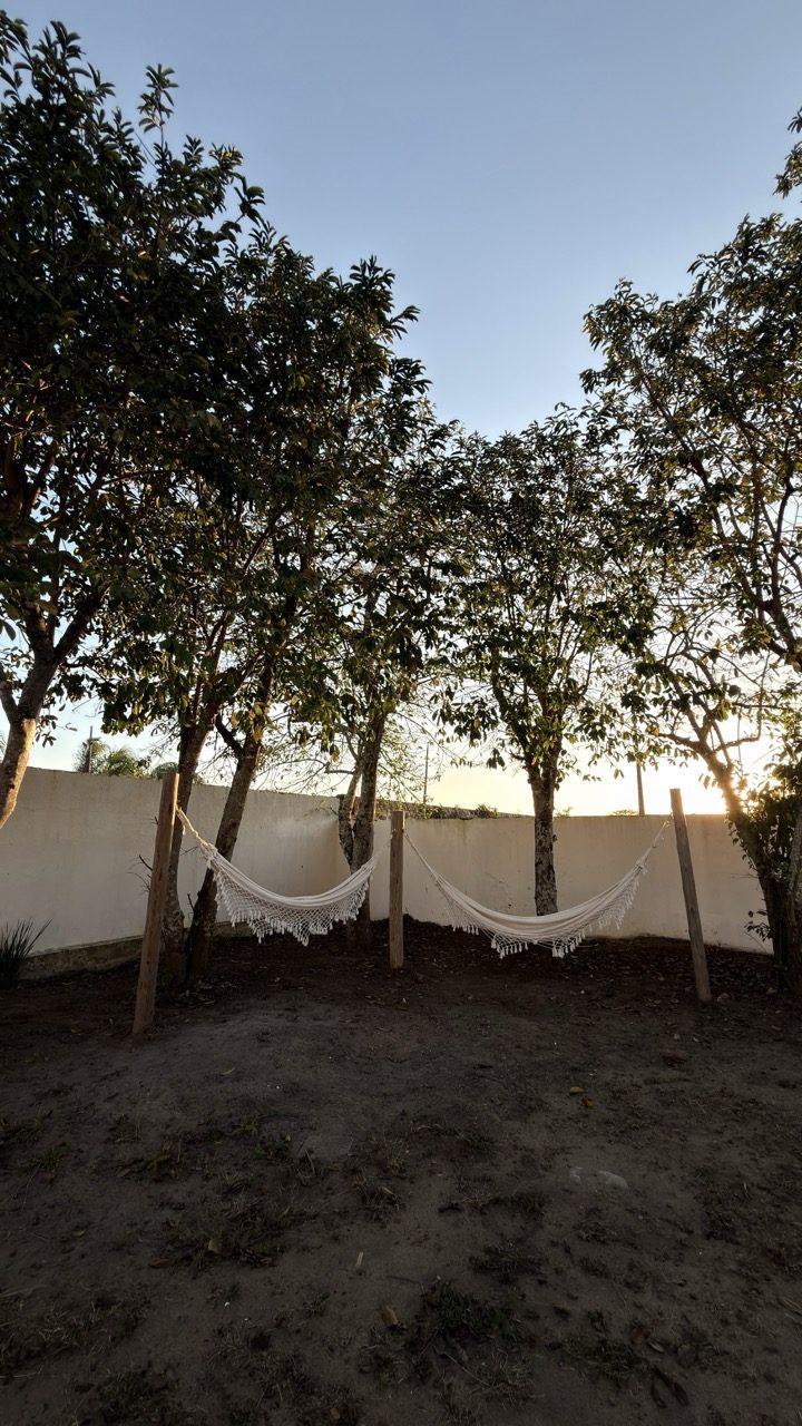 Duas redes brancas armadas entre árvores no quintal do hotel, ao fim da tarde