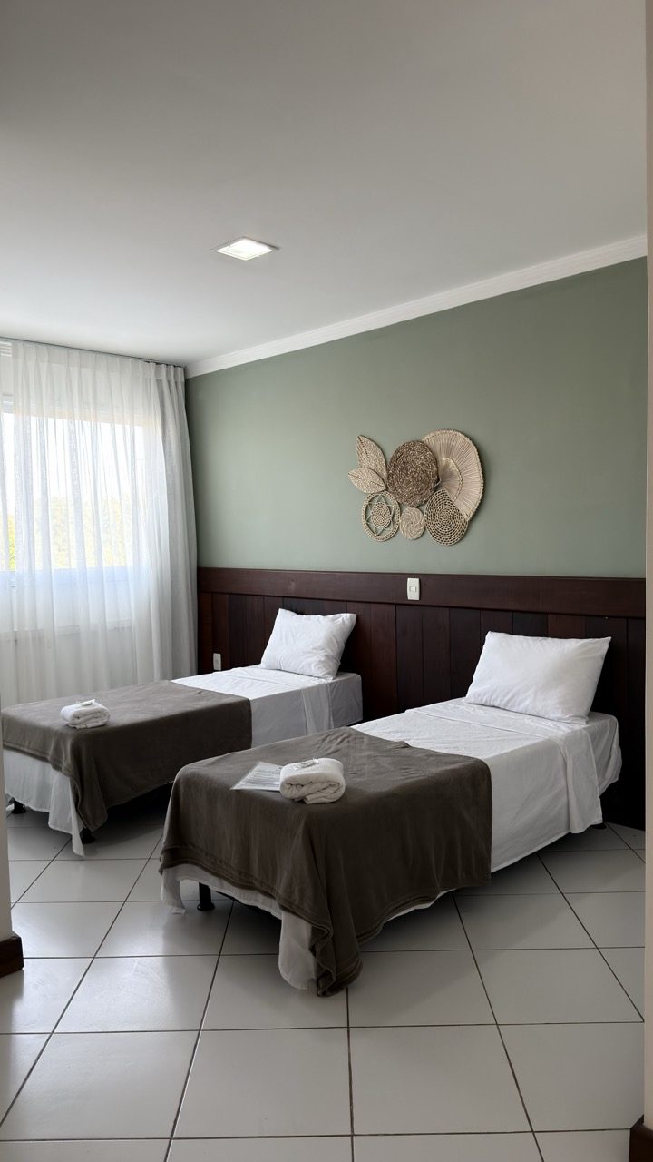 Quarto com camas de solteiro, parede verde sálvia e piso claro